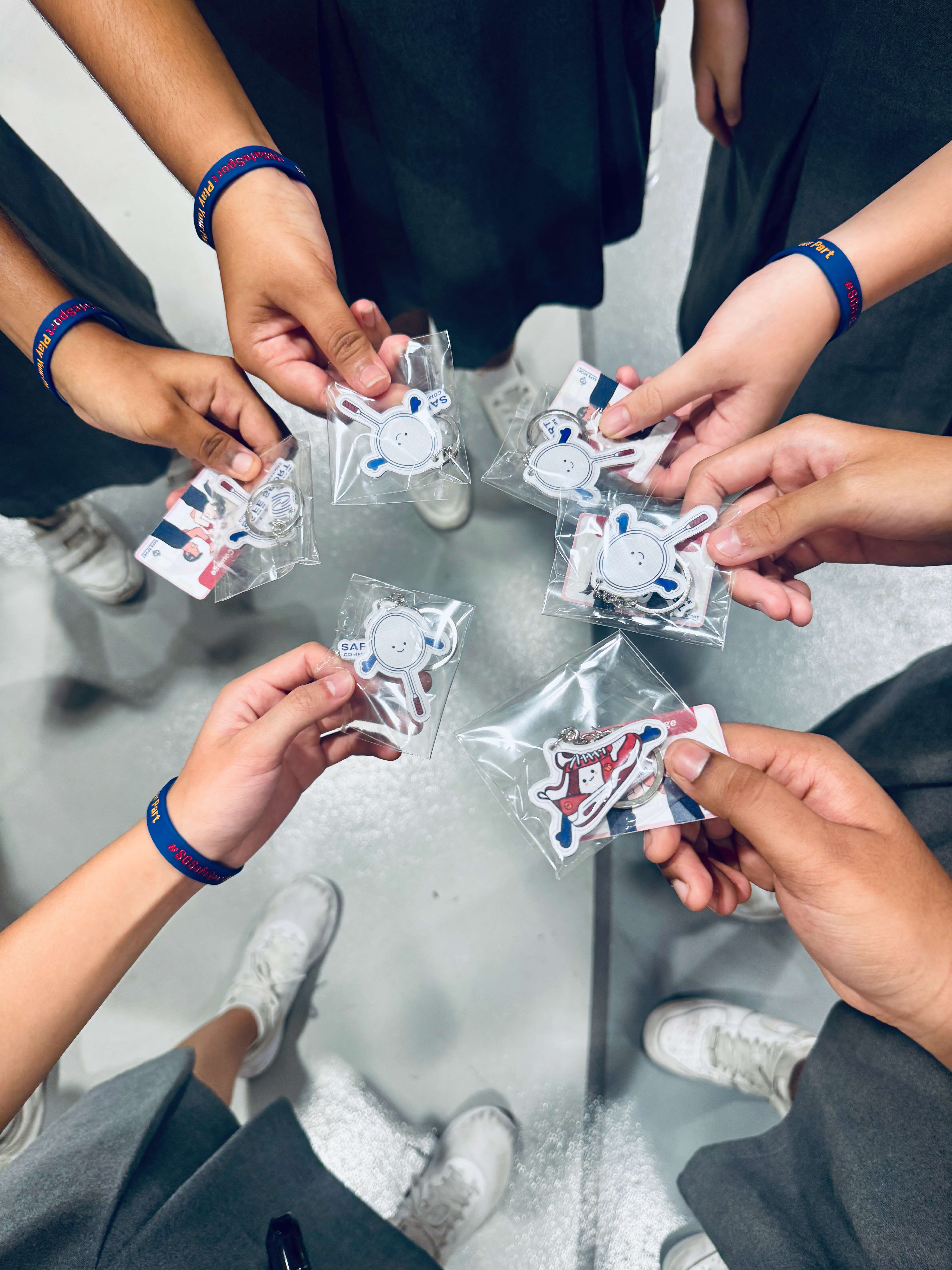 Six hands holding up keychains in the centre, forming a circle
