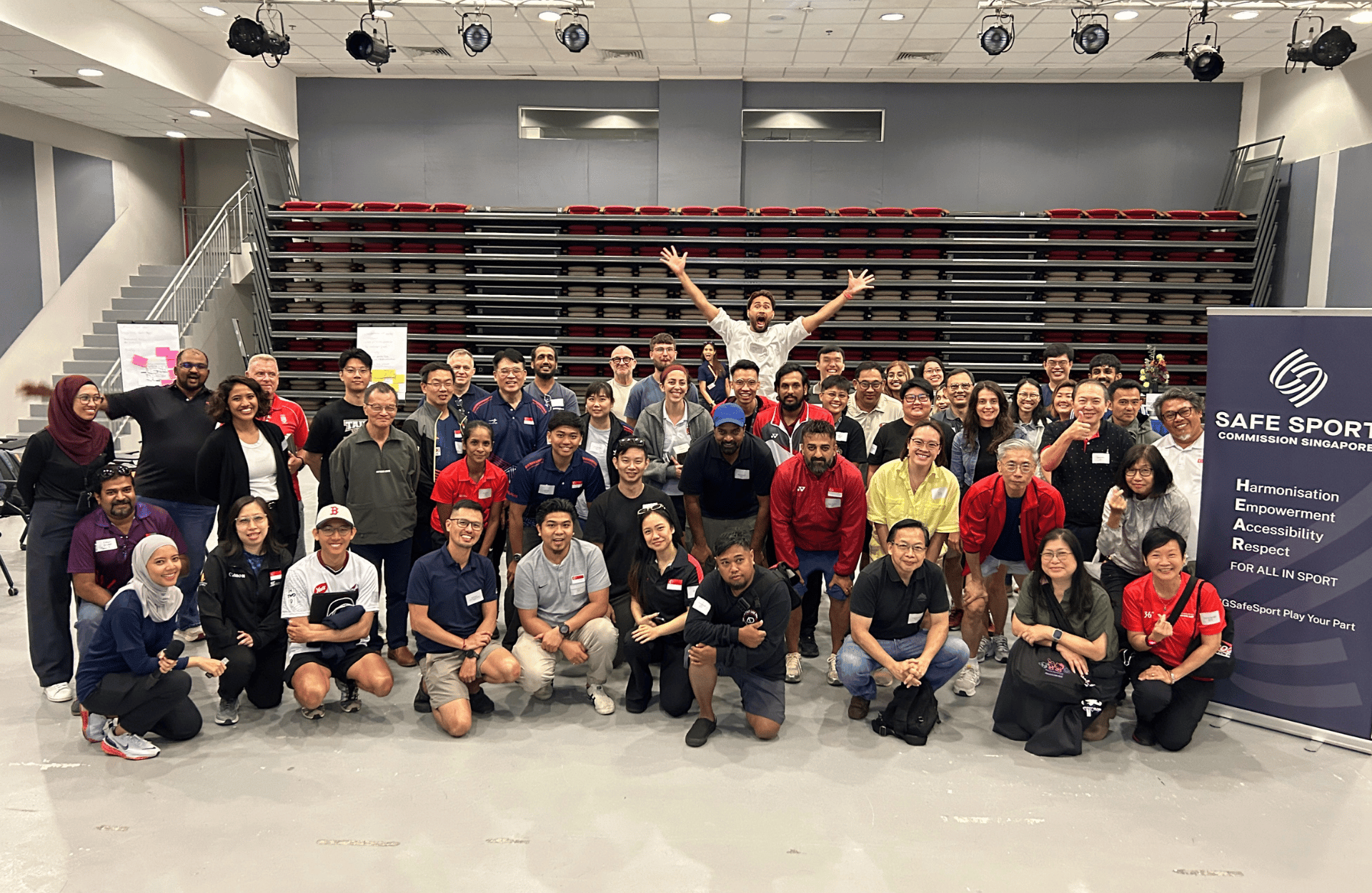 Group photo of diverse individuals in a spacious room, smiling widely