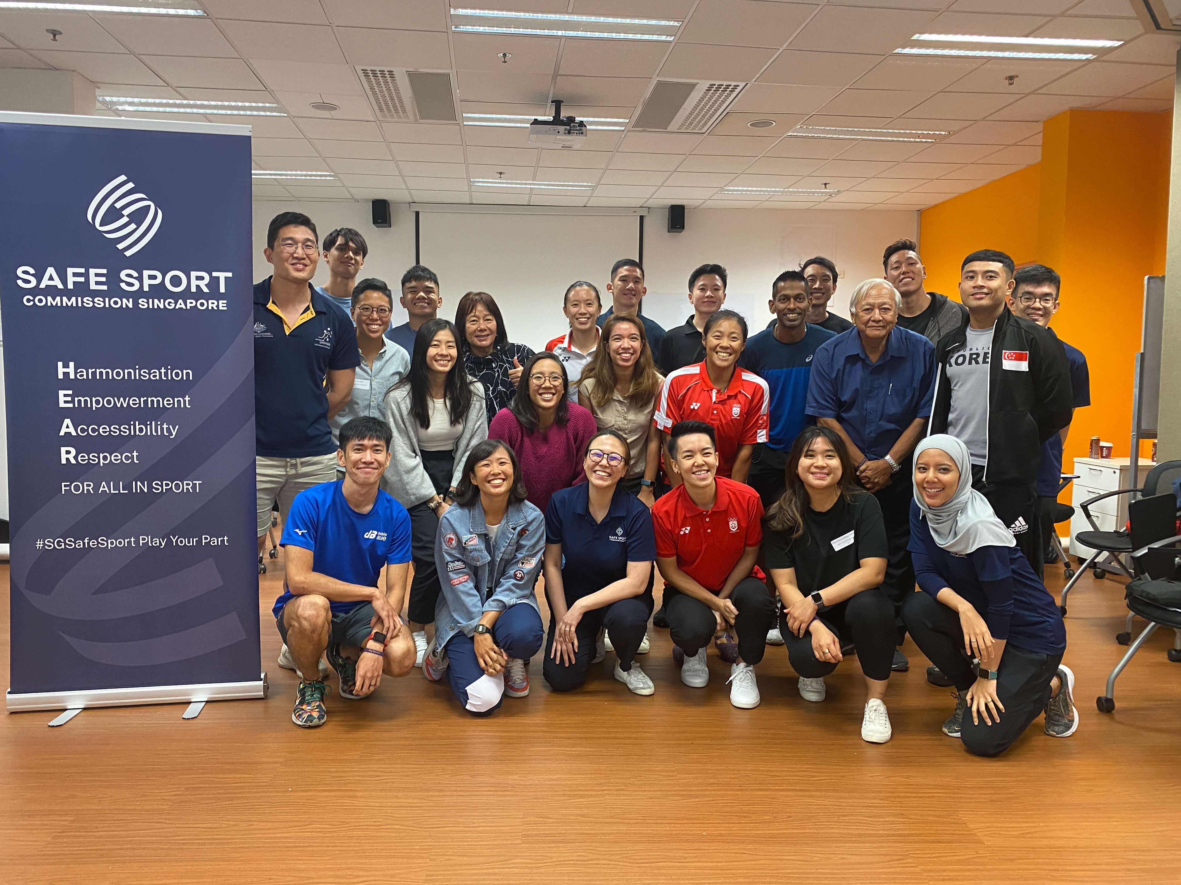 Trainers and participants pose for a photo next to a navy blue Safe Sport pull up banner